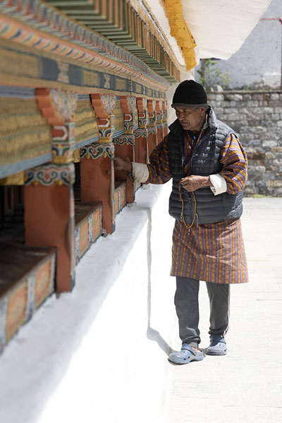 Foto van Old man in Bhutanese clothes turning the prayer wheels around the Chorten KoraTrashiyangtse Chorten Kora - Bhutan