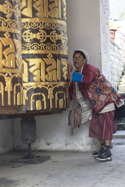 Foto di Old Bhutanese woman in traditional garb setting a huge prayer wheel in motionTrashiyangtse Chorten Kora - Bhutan