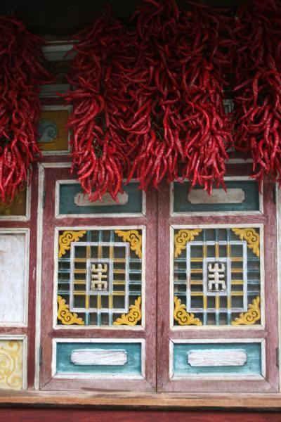 Picture of Jiaju Tibetan village (China): Red peppers hanging under the roof of a richly decorated window