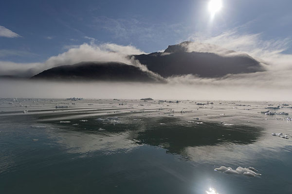 Sun shining over Qooroq fjord with clouds over the mountain and icebergs in the water | Fjord de Qooroq | 