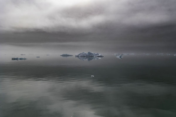 Foto van Icebergs in the fjord under a sky with dark cloudsQooroq fjord - 