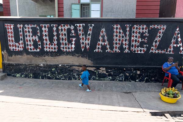 Man watching a child walk by a slogan saying Ubugwaneza, or Generosity | Nyamirambo community | Rwanda